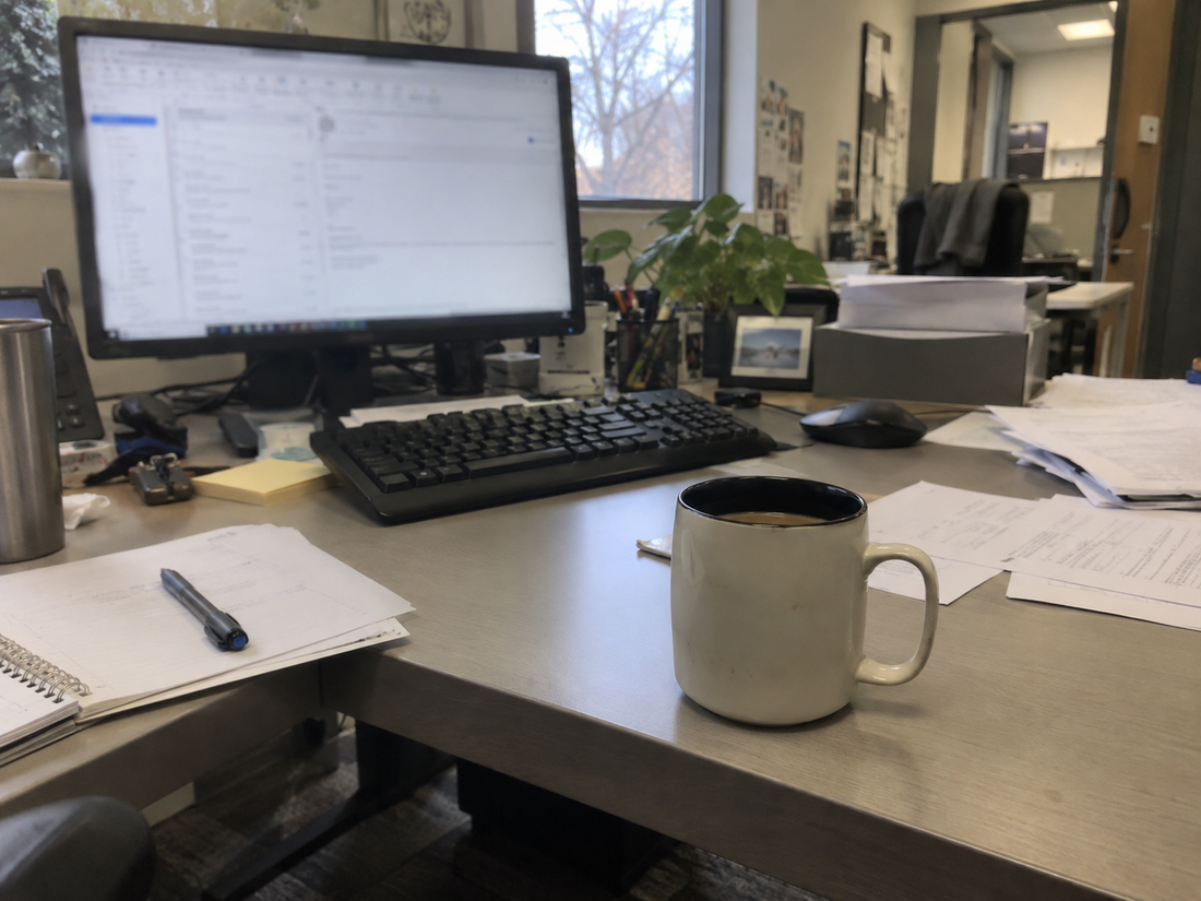 An office desk in the afternoon with a monitor and a half-finished coffee